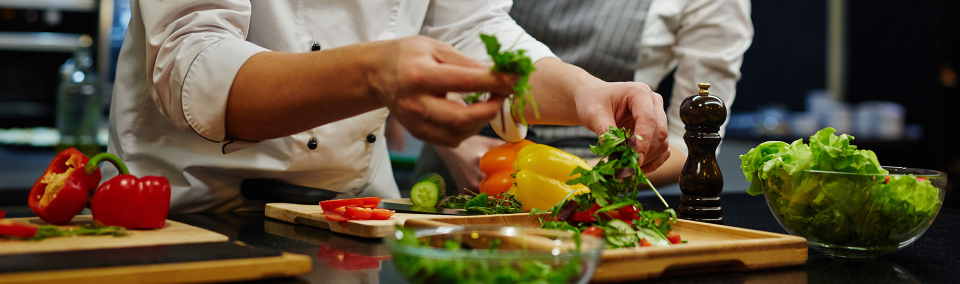 Chef en cuisine qui est en train de montrer à son commis comment cuisiner les légumes