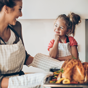 Una mamá y su hija pequeña cocinan juntas un pollo entero Doux