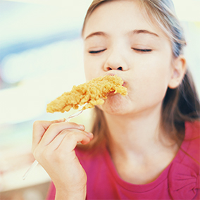 Little girl eating a Doux chicken tender with breaded coating