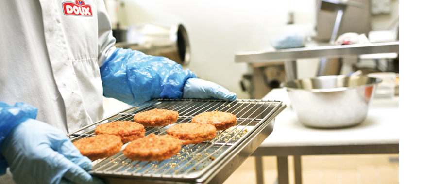 Photo of a person putting breaded burgers on a grill